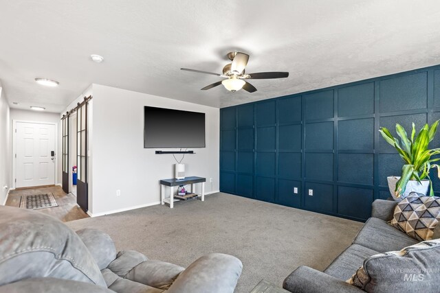 carpeted living area with a decorative wall, a ceiling fan, and baseboards
