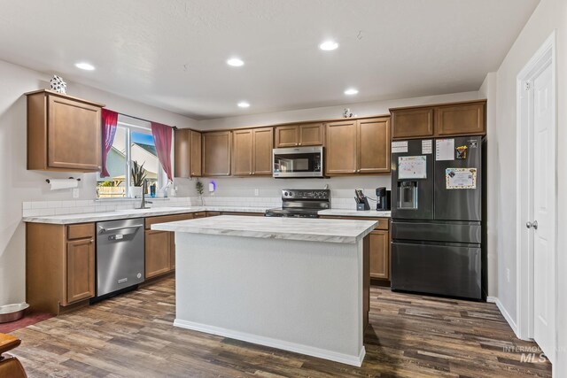 kitchen with appliances with stainless steel finishes, light countertops, recessed lighting, a kitchen island, and dark wood-style flooring