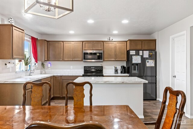 kitchen with black appliances, a sink, recessed lighting, brown cabinets, and wood finished floors