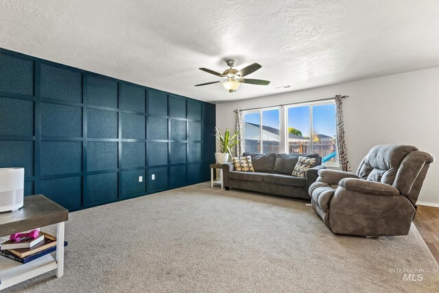 carpeted living area with a decorative wall, a ceiling fan, and a textured ceiling