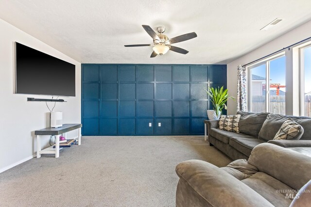 carpeted living area with a decorative wall, a ceiling fan, and baseboards