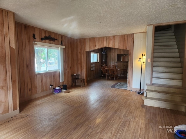 82 NW 3rd St, Ontario, OR 97914 - unfurnished living room with a textured ceiling, stairs, light wood-style floors, and wooden walls