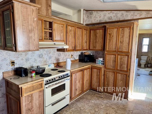 kitchen with white electric range oven, under cabinet range hood, light countertops, wallpapered walls, and brown cabinetry