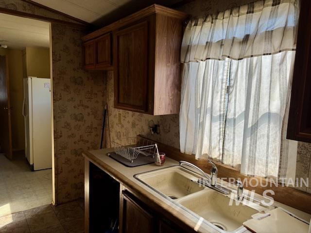 kitchen featuring freestanding refrigerator, wallpapered walls, light countertops, a sink, and lofted ceiling