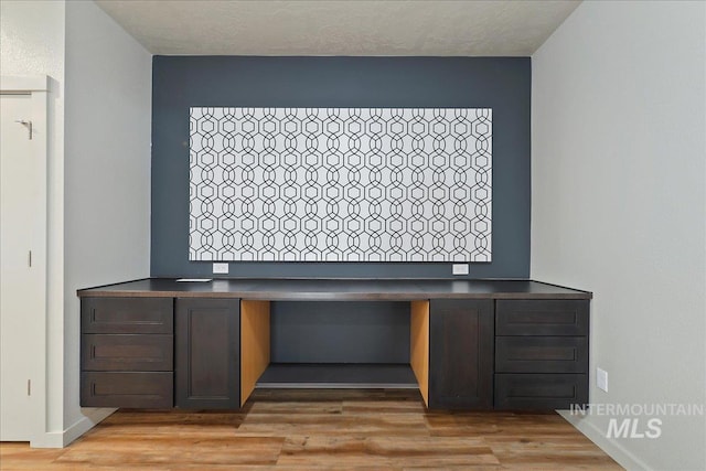 unfurnished office featuring built in desk, light hardwood / wood-style flooring, and a textured ceiling