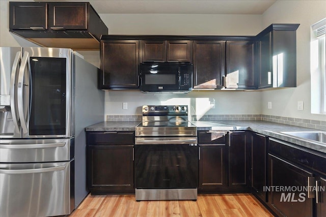 kitchen with appliances with stainless steel finishes, stone countertops, sink, dark brown cabinetry, and light wood-type flooring