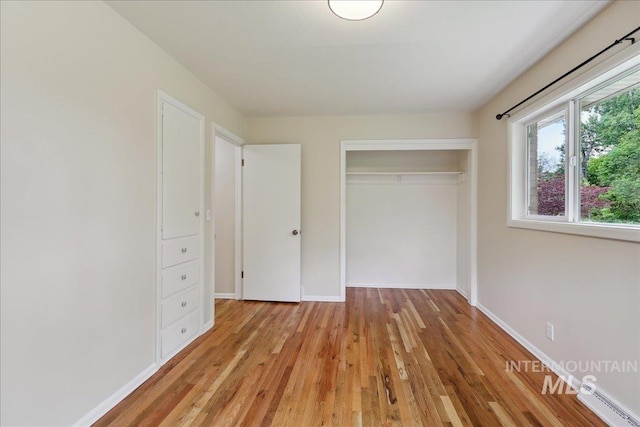 unfurnished bedroom featuring a baseboard heating unit, a closet, light wood-type flooring, and baseboards