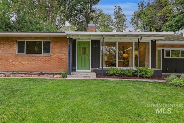 single story home with a chimney, a front yard, and brick siding