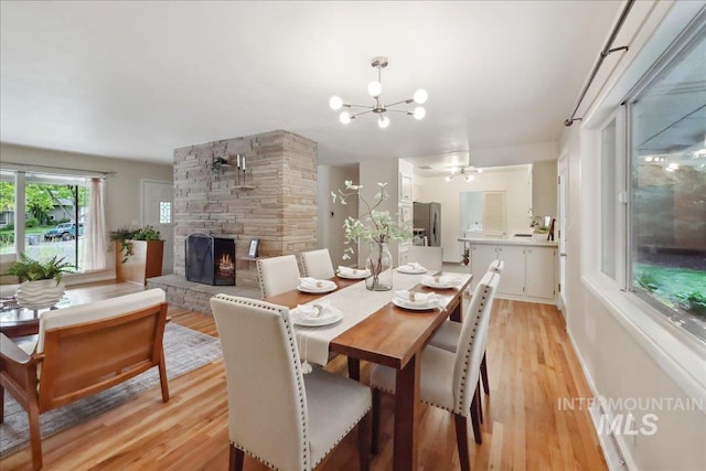 dining room with light wood-type flooring, a chandelier, and a stone fireplace