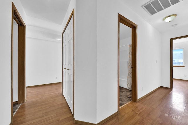 hall with baseboards, visible vents, and light wood finished floors