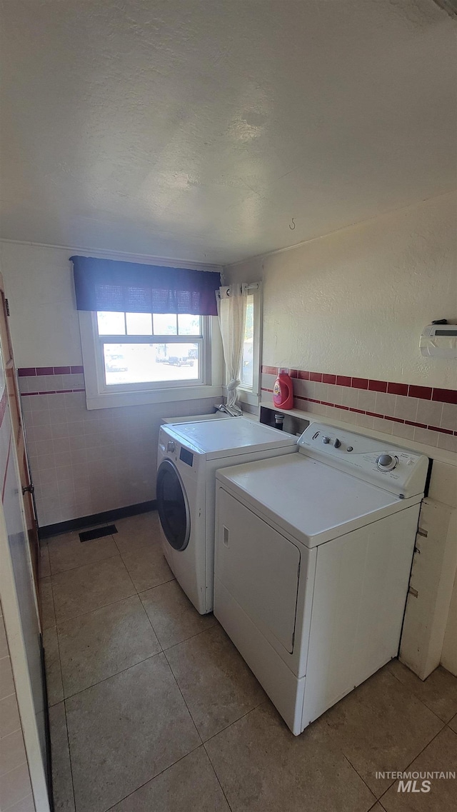 laundry room with tile walls, light tile patterned floors, and washing machine and dryer