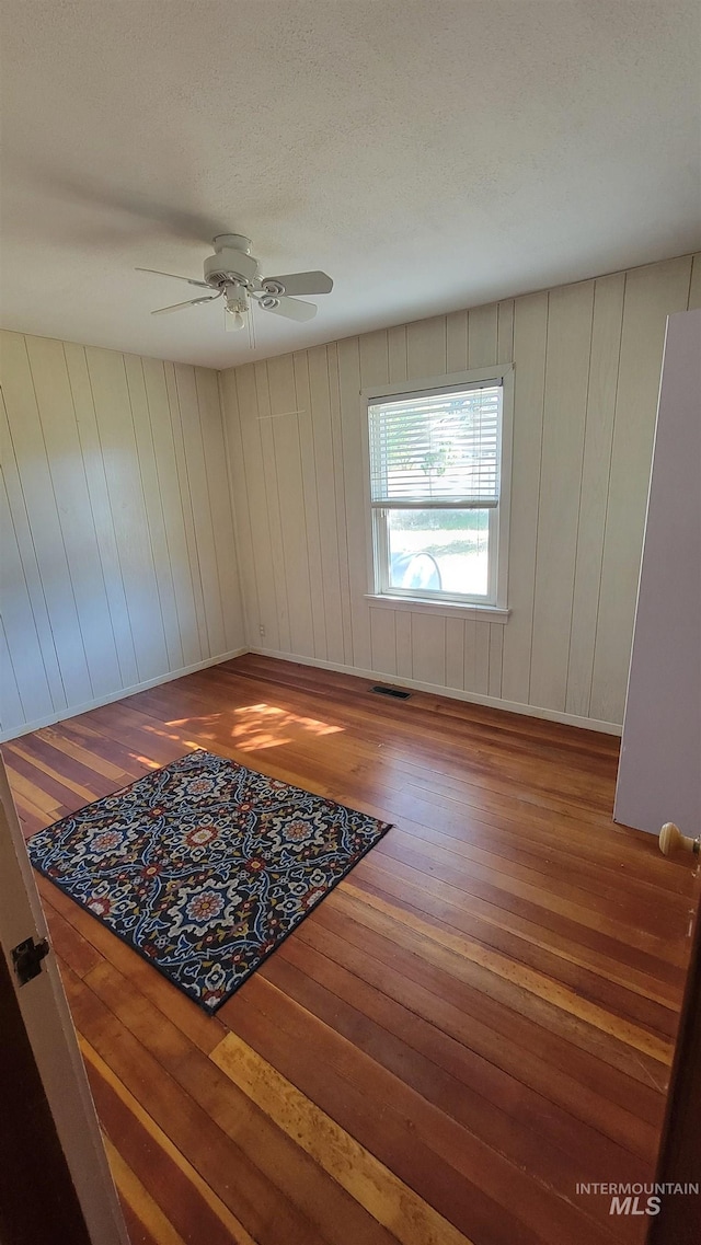 spare room with wood-type flooring, wooden walls, and ceiling fan