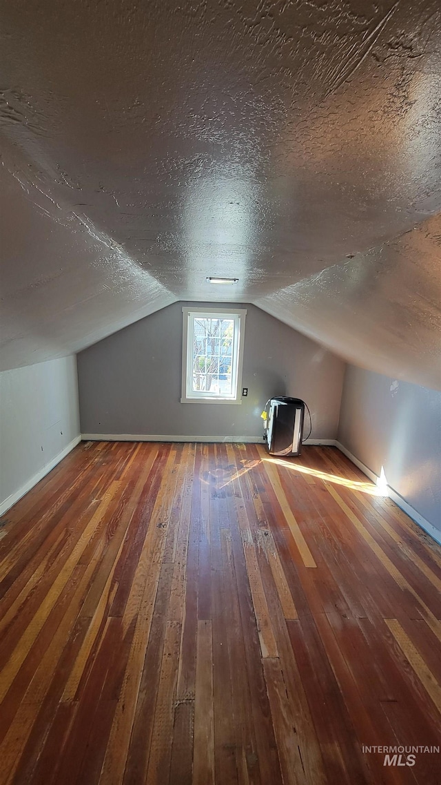 additional living space featuring wood-type flooring, a textured ceiling, and vaulted ceiling