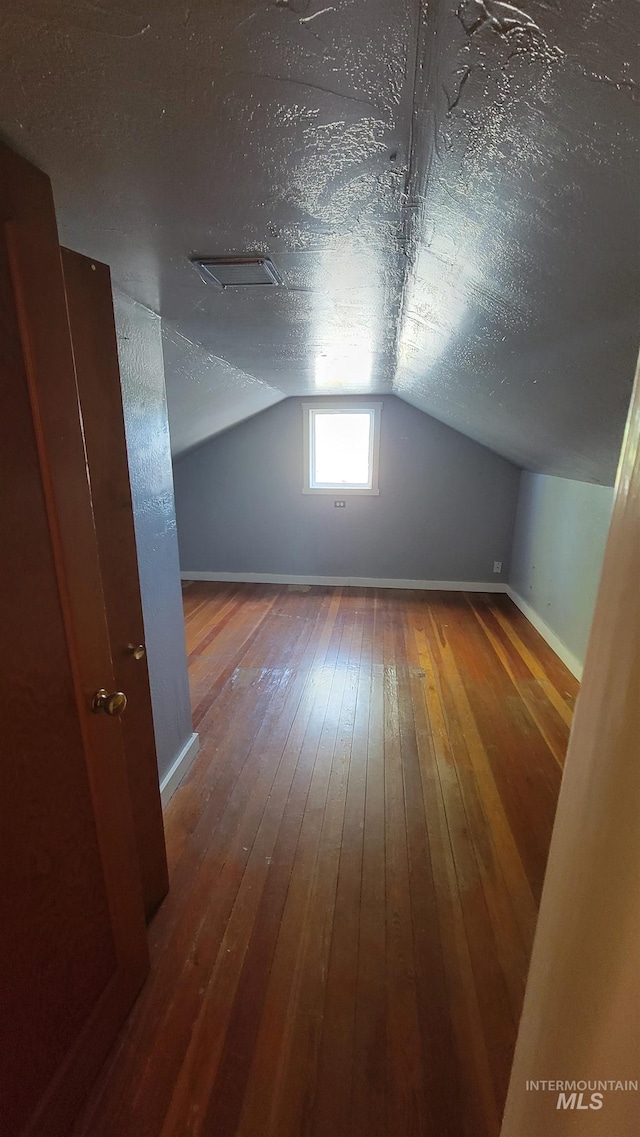 additional living space with a textured ceiling, wood-type flooring, and lofted ceiling