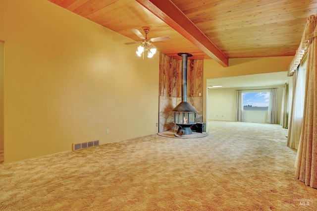 unfurnished living room with carpet, wood ceiling, ceiling fan, beamed ceiling, and a wood stove