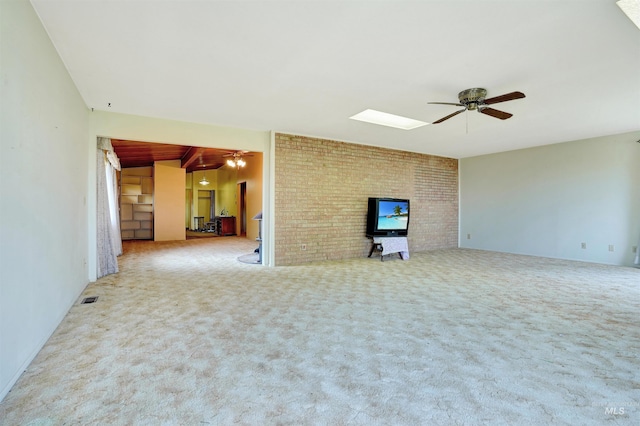 unfurnished living room with a skylight, ceiling fan, beamed ceiling, light colored carpet, and brick wall