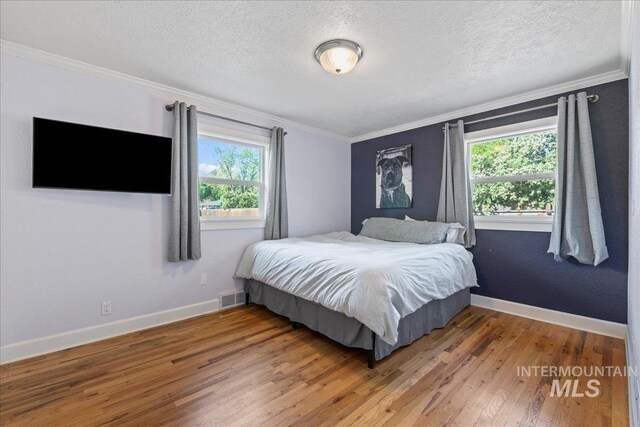 bedroom featuring visible vents, ornamental molding, wood finished floors, and multiple windows