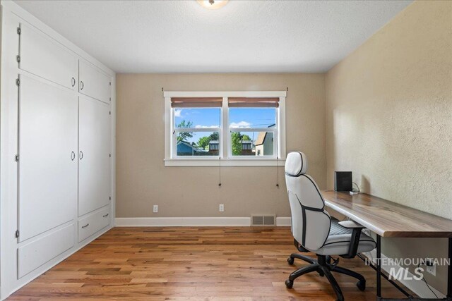 office with baseboards, visible vents, a textured wall, and light wood-type flooring