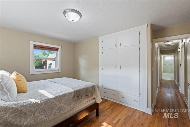 bedroom with a closet, baseboards, a textured ceiling, and wood finished floors
