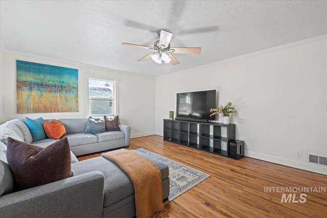 living room with ceiling fan, baseboards, wood finished floors, visible vents, and ornamental molding