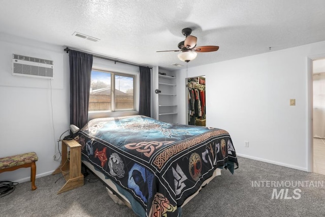 bedroom with carpet flooring, a wall mounted air conditioner, a textured ceiling, baseboards, and visible vents