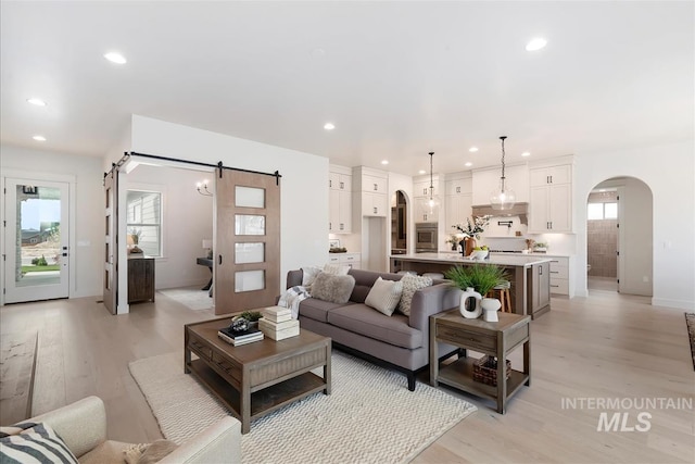 living room with a barn door, arched walkways, baseboards, light wood-style flooring, and recessed lighting