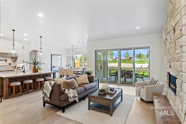 living area with light wood finished floors, recessed lighting, a fireplace, and an inviting chandelier