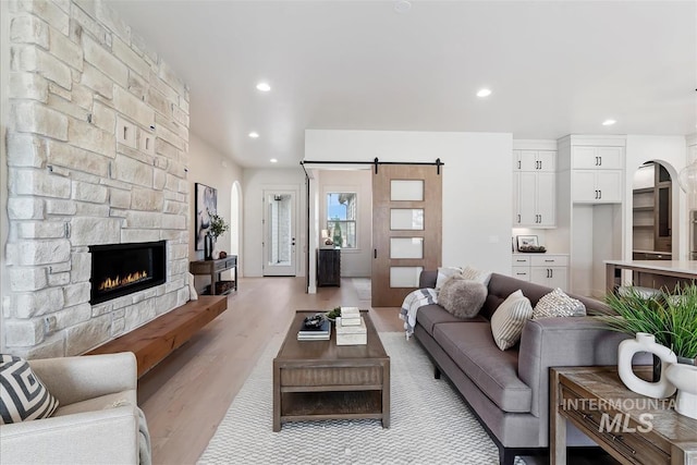 living room with arched walkways, a barn door, recessed lighting, a fireplace, and light wood finished floors