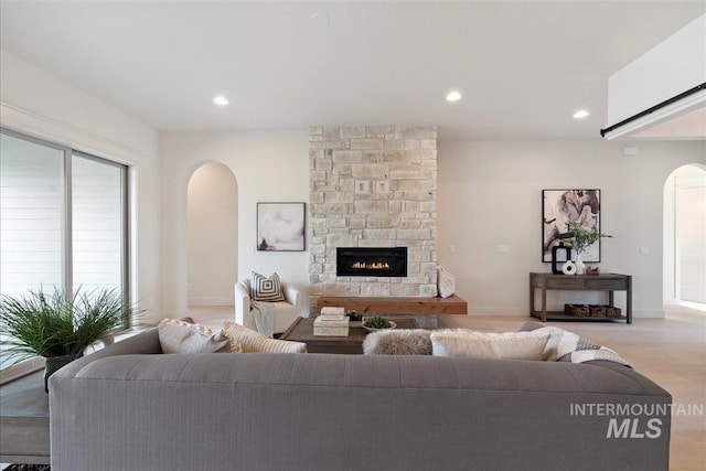 living room with arched walkways, a stone fireplace, light wood-style flooring, and recessed lighting