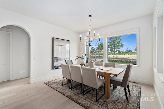 dining area featuring arched walkways, baseboards, a notable chandelier, and light wood finished floors