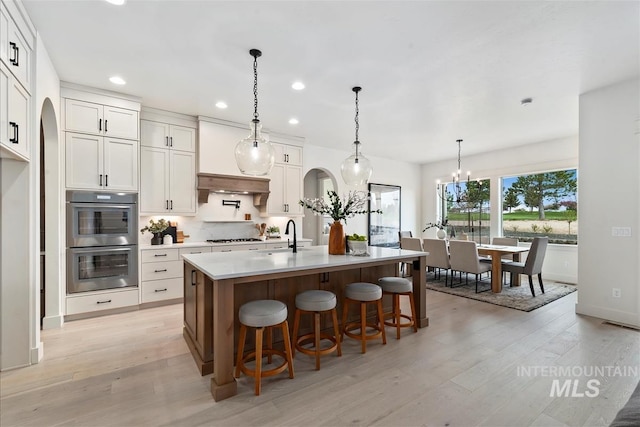 kitchen with light countertops, stainless steel double oven, backsplash, and light wood-style flooring