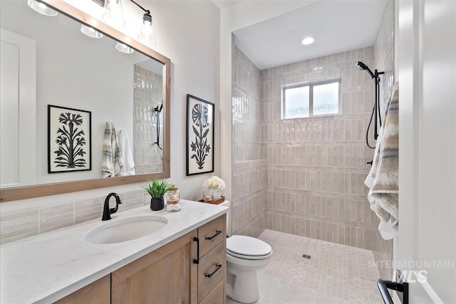 bathroom with toilet, tiled shower, and vanity