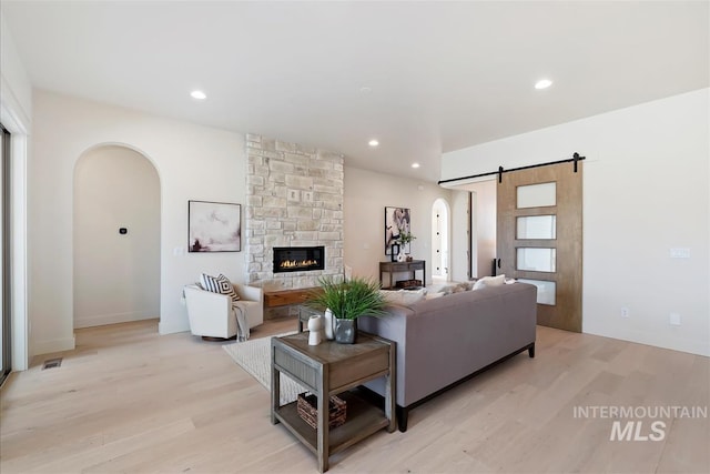 living room featuring light wood-style floors, arched walkways, a fireplace, and a barn door