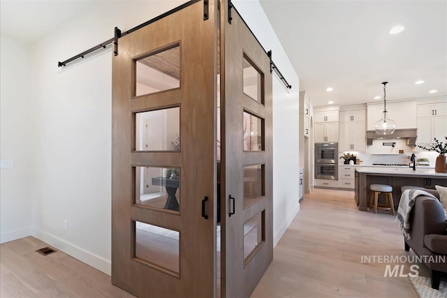 hallway with a barn door, recessed lighting, visible vents, baseboards, and light wood finished floors