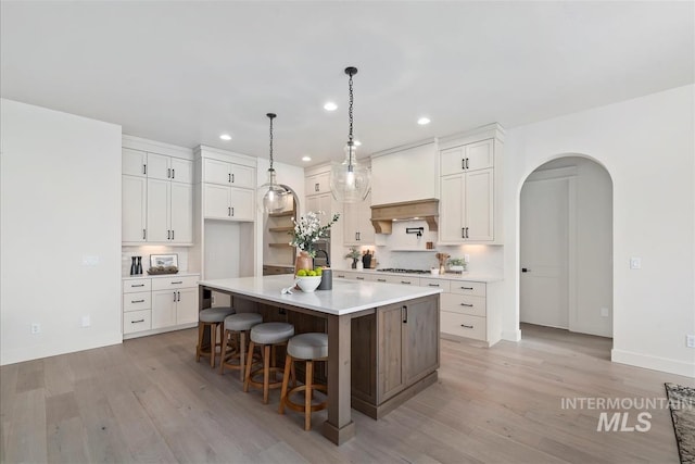 kitchen featuring arched walkways, white cabinets, a spacious island, light wood-style flooring, and premium range hood