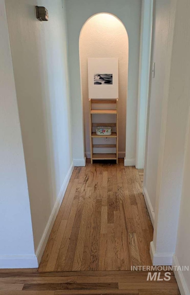 corridor featuring light wood-style flooring, arched walkways, and baseboards