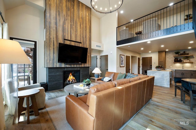 living room with a towering ceiling, sink, a chandelier, a tiled fireplace, and light hardwood / wood-style flooring