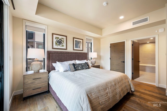 bedroom with ensuite bath, dark wood-type flooring, and a raised ceiling