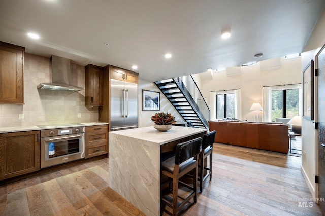 kitchen featuring wall chimney exhaust hood, a breakfast bar area, light hardwood / wood-style flooring, appliances with stainless steel finishes, and a kitchen island