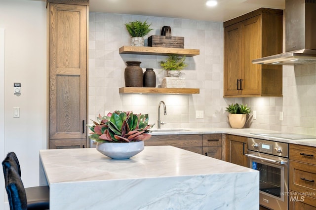 kitchen featuring wall chimney range hood, tasteful backsplash, sink, and stainless steel oven