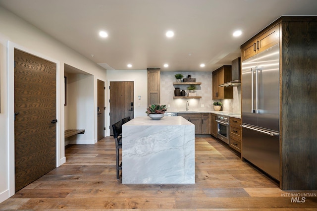 kitchen featuring appliances with stainless steel finishes, sink, light wood-type flooring, and wall chimney exhaust hood