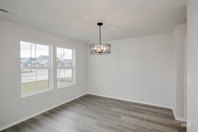 unfurnished room featuring a notable chandelier, baseboards, visible vents, and wood finished floors