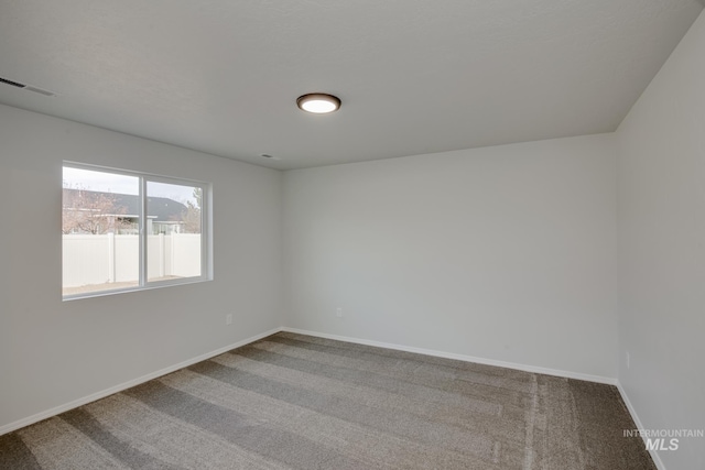 empty room with carpet, visible vents, and baseboards