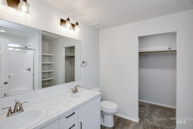 bathroom featuring toilet, a sink, a shower with shower door, and a walk in closet