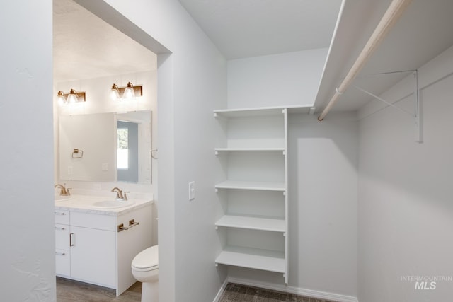 bathroom with double vanity, toilet, a sink, wood finished floors, and baseboards