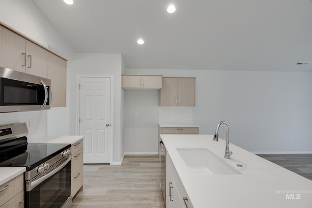 kitchen featuring stainless steel appliances, light wood-type flooring, light countertops, and a sink