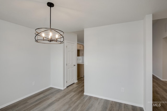 unfurnished dining area featuring an inviting chandelier, baseboards, and wood finished floors