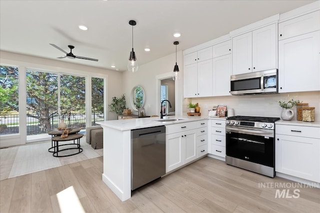 kitchen with a peninsula, stainless steel appliances, light wood-style floors, white cabinetry, and a sink