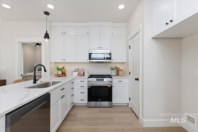 kitchen featuring light stone countertops, a sink, appliances with stainless steel finishes, white cabinetry, and backsplash