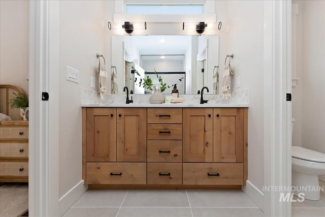 bathroom featuring baseboards, double vanity, a sink, tile patterned flooring, and toilet